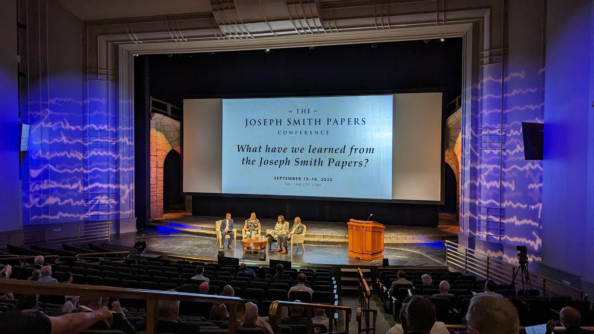 JSP staff onstage at the Joseph Smith Papers conference while audience looks on from their seats